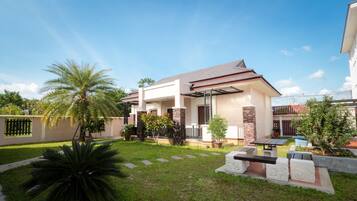 A modern two-story house with a covered patio, a well-maintained lawn, and a variety of potted plants.