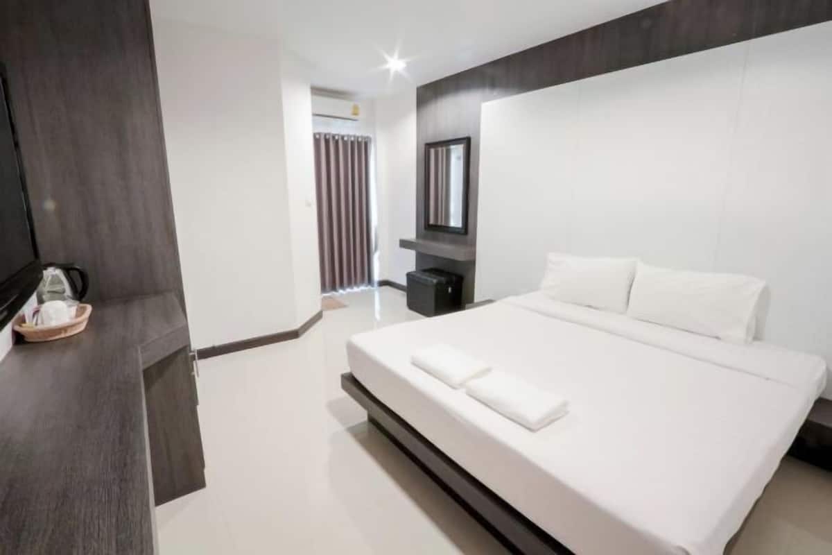 A modern hotel room with a large bed, a flat-screen TV, a dark wood panel, and a small table with a basket.
