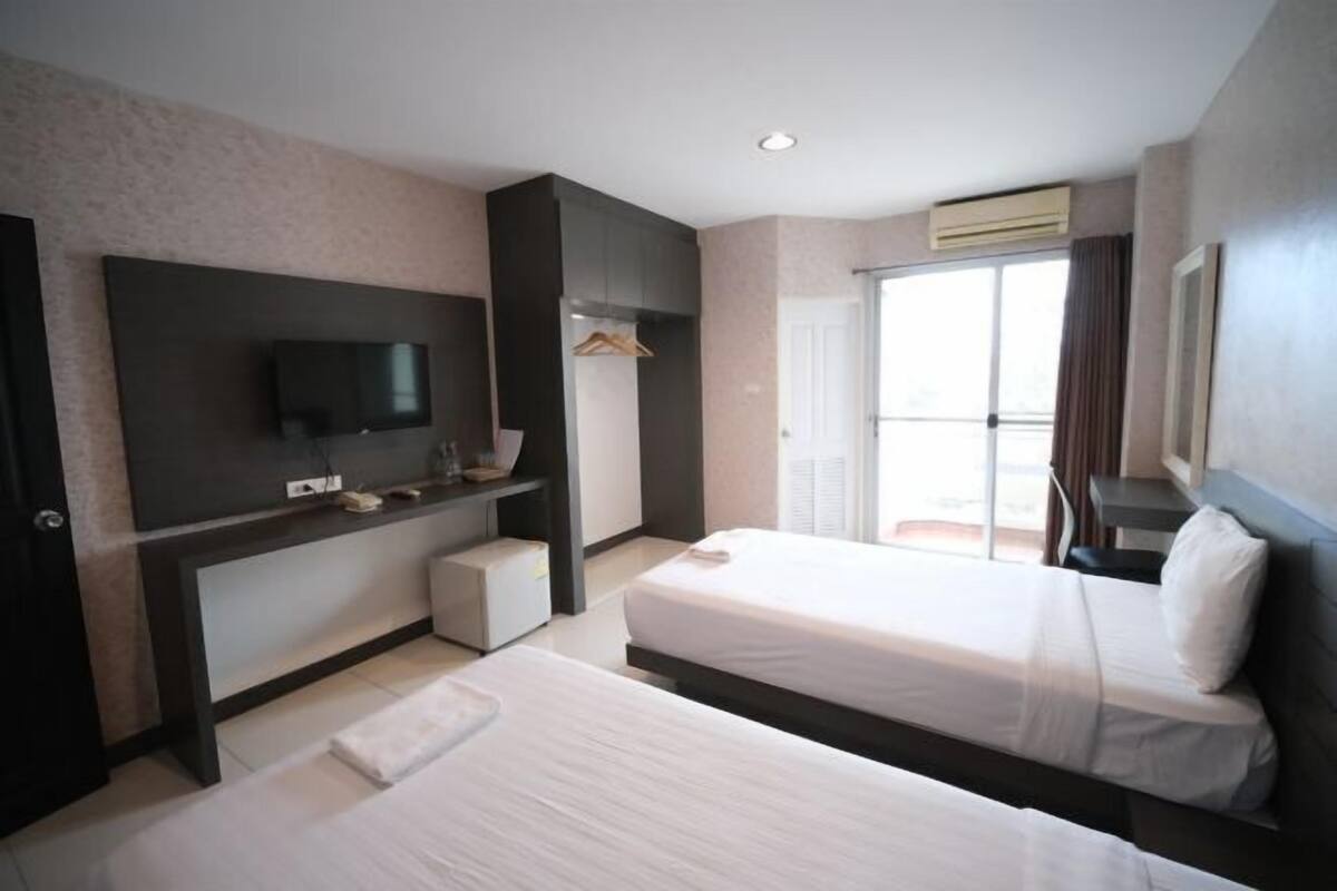 Habitación de hotel con dos camas, un televisor, un escritorio y una ventana con cortinas.