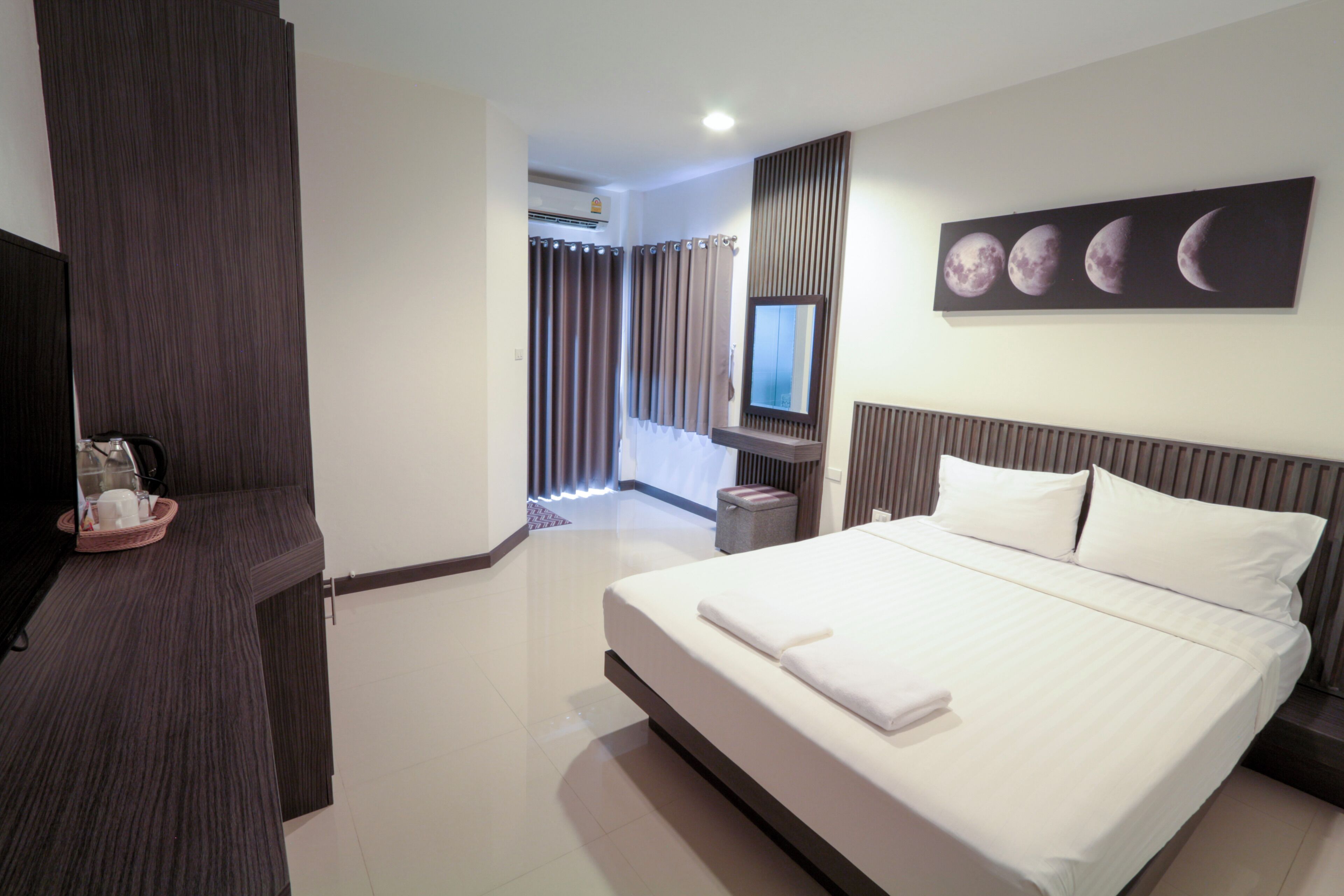 A modern hotel room with a large bed, a flat-screen TV, a wall-mounted mirror, and a painting of the moon phases.