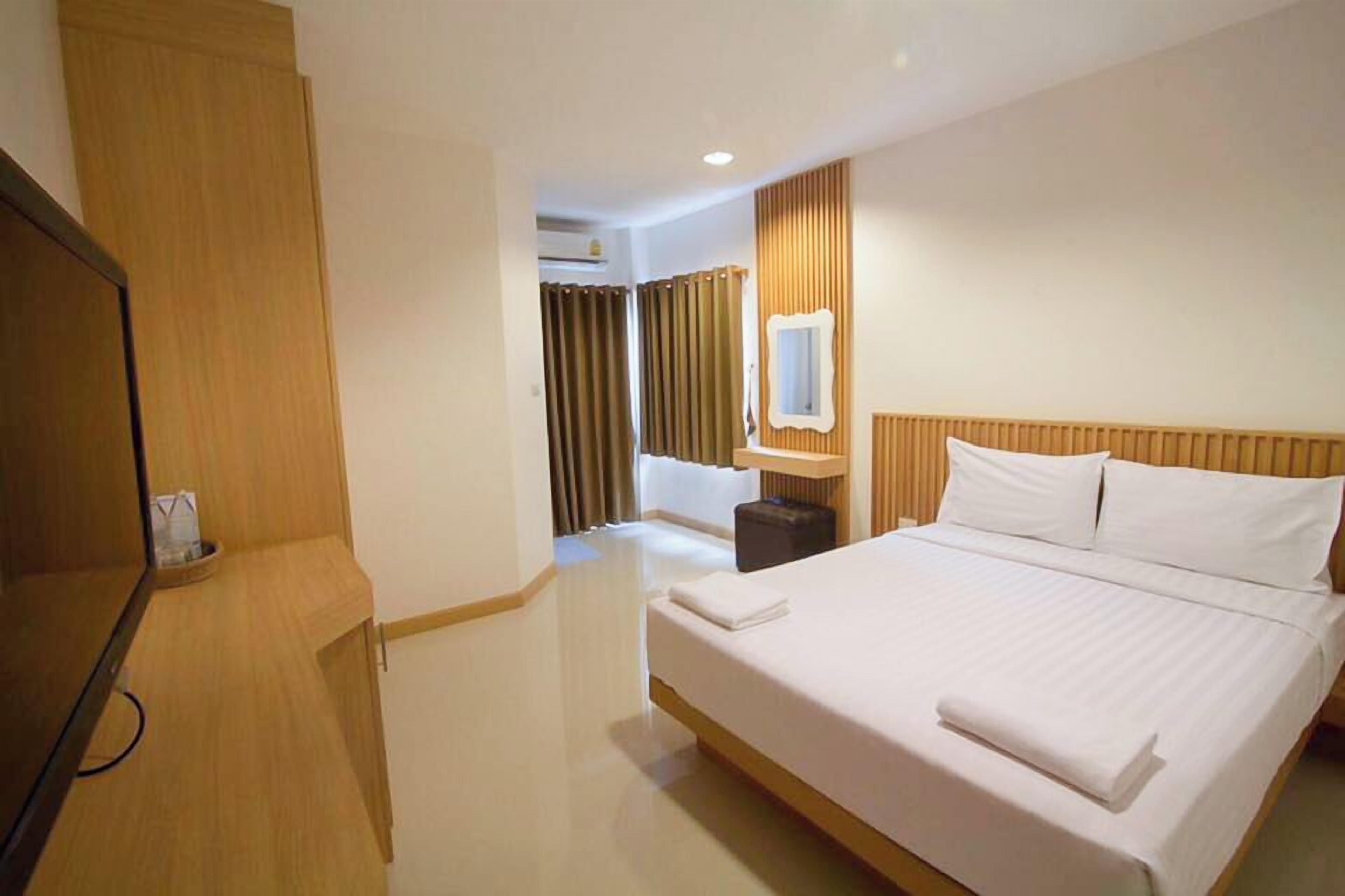 A hotel room with a bed, a TV, a wooden wardrobe, and a bathroom visible through a door.