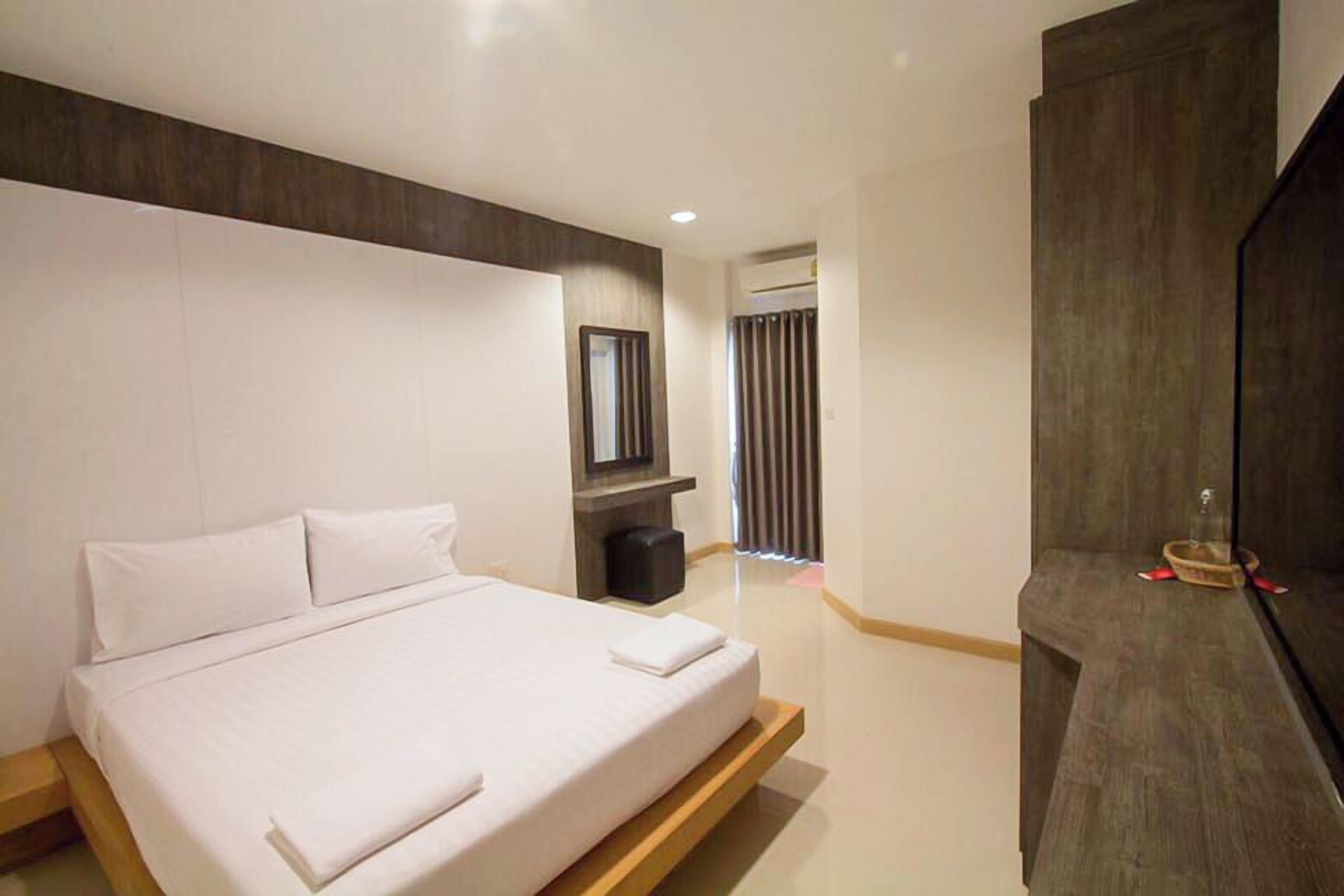 A modern hotel room with a large bed, a TV, and a wooden side table.