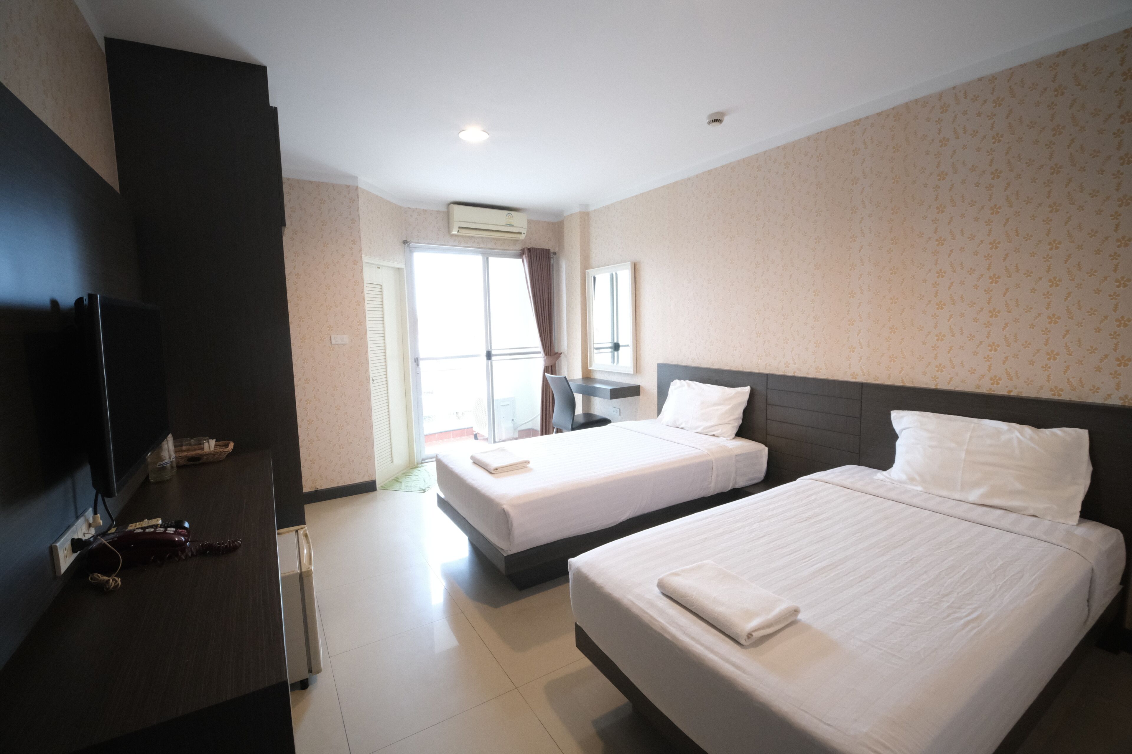 A hotel room with two beds, a TV, a desk, and a window.