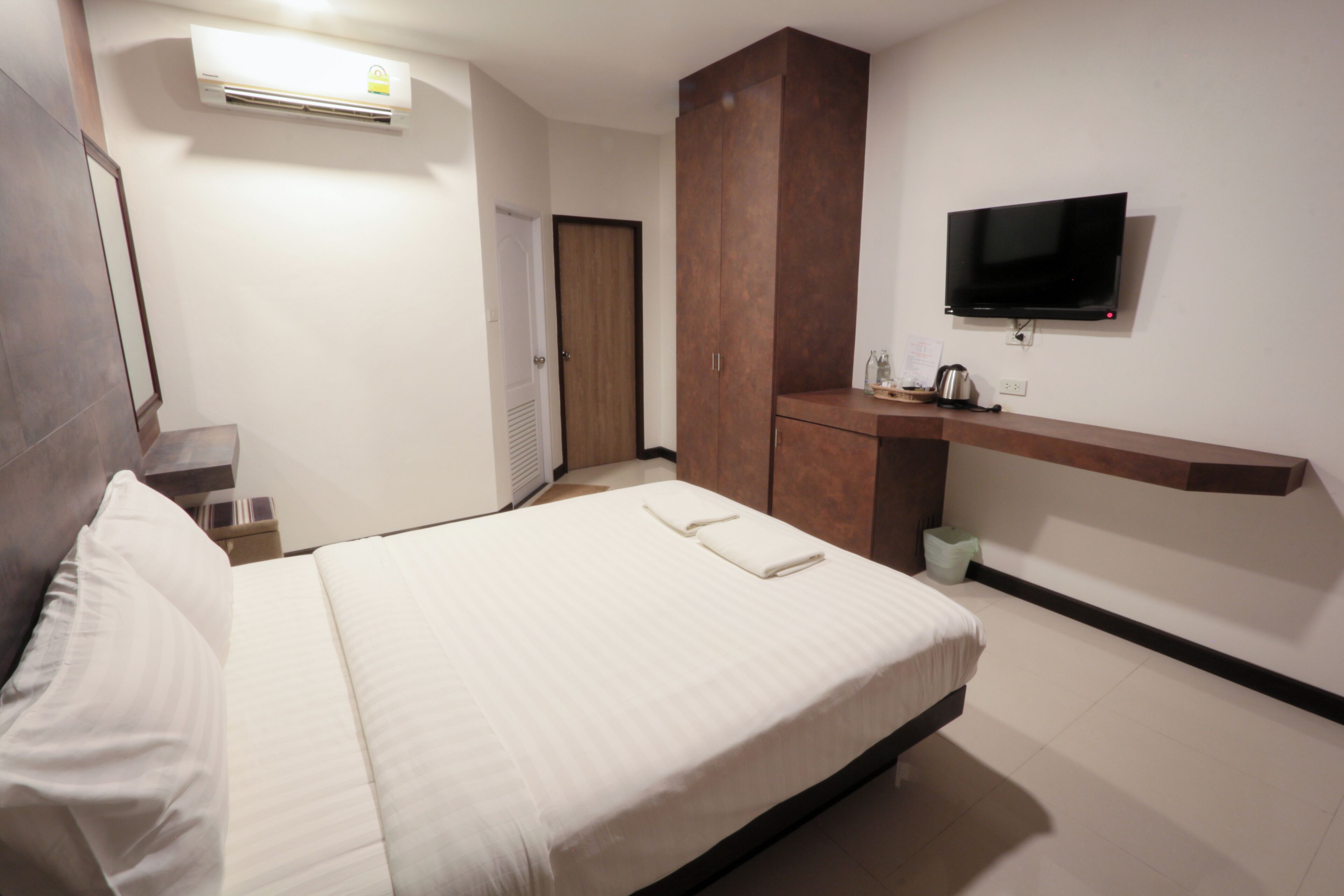 A hotel room with a bed, a TV mounted on the wall, a wardrobe, and a small kitchenette area.