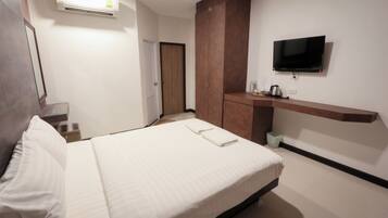 A hotel room with a bed, a TV mounted on the wall, a wardrobe, and a small kitchenette area.