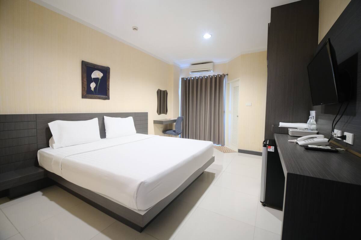 Una habitación de hotel con cama, escritorio, teléfono, televisión y aire acondicionado.