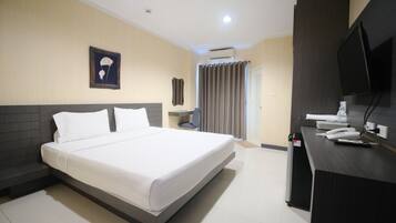 A hotel room with a bed, a desk with a telephone, a television, and an air conditioning unit.