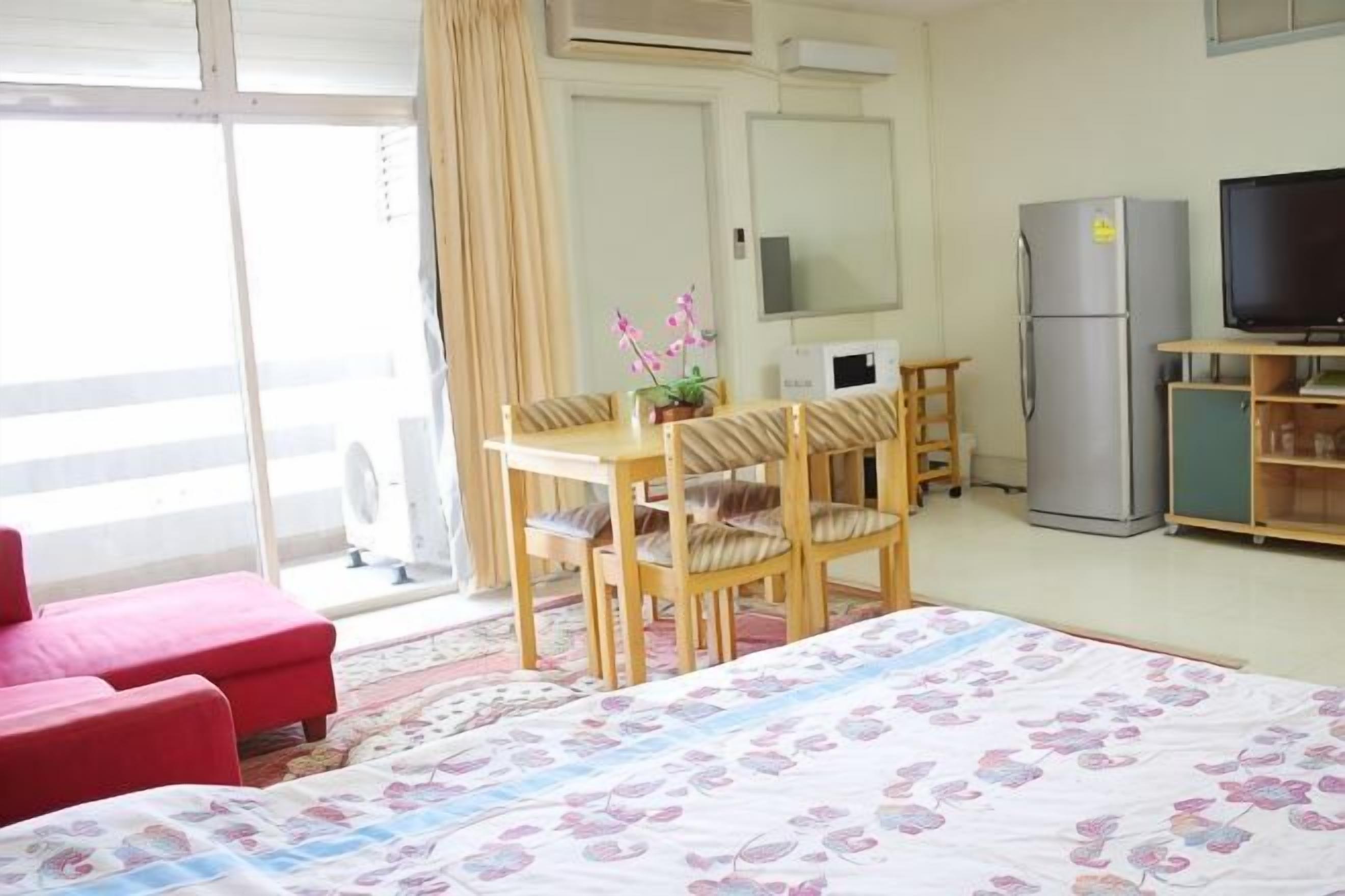 Una habitación de hotel con cama, escritorio con sillas, refrigerador, televisión y puerta corrediza de vidrio.