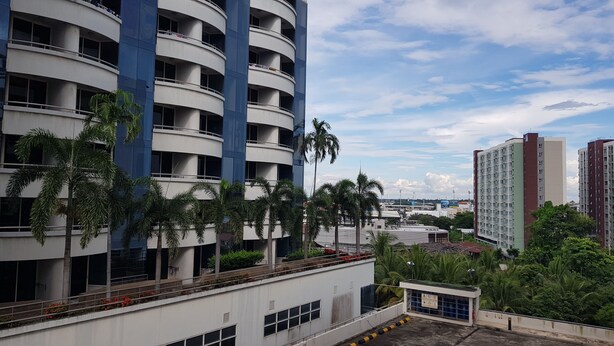 A multi-story building with balconies, surrounded by palm trees and other greenery. - Aek Udon Apartment (Udon Thani)