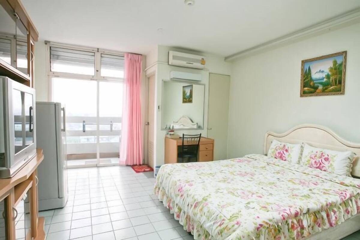 A bedroom with a bed, a desk, a chair, a television, and a balcony with a view.