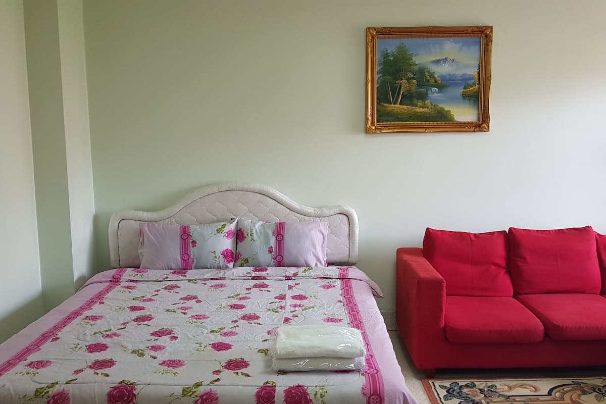 A bedroom with a bed, a red sofa, and a painting on the wall.