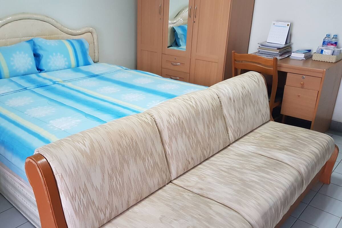 A bedroom with a bed, a wooden wardrobe, a desk, and a chair.