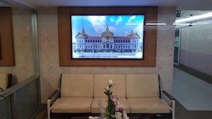 A reception area with a sofa, a framed picture of a building, and a floral wall design. - Aek Udon Apartment (Udon Thani)