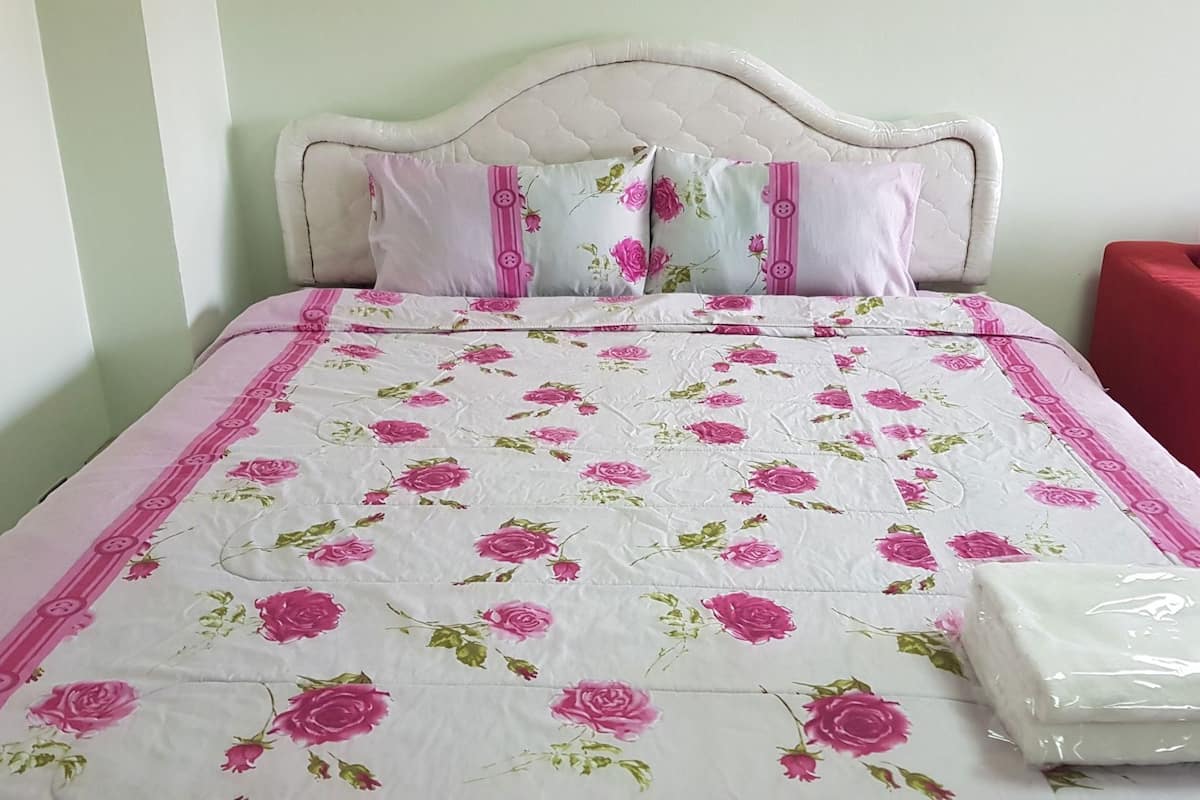 A bed with a floral bedspread, pillows with a pink and white pattern, and a red chair.