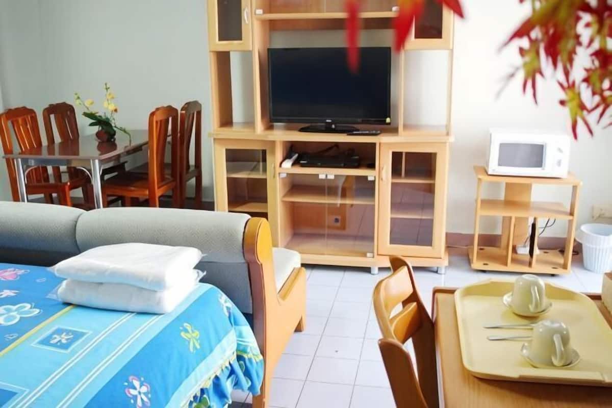 Una habitación con cama, televisión, microondas, mesa de comedor con sillas y una mesita con tazas y bandeja.