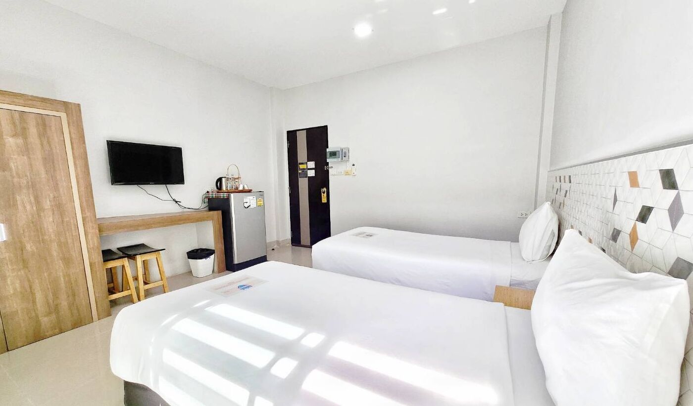 A hotel room with two beds, a TV, a minibar, and a wooden door.