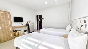 A hotel room with two beds, a TV, a minibar, and a wooden door.