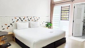 A neatly made bed with white bedding, a small wooden table with a chair, and a potted plant on the nightstand. - Thanaphat Place (Lam Plai Mat)