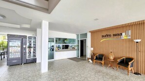 A reception area with a wooden wall, two chairs, a reception desk, and vending machines. - Thanaphat Place (Lam Plai Mat)