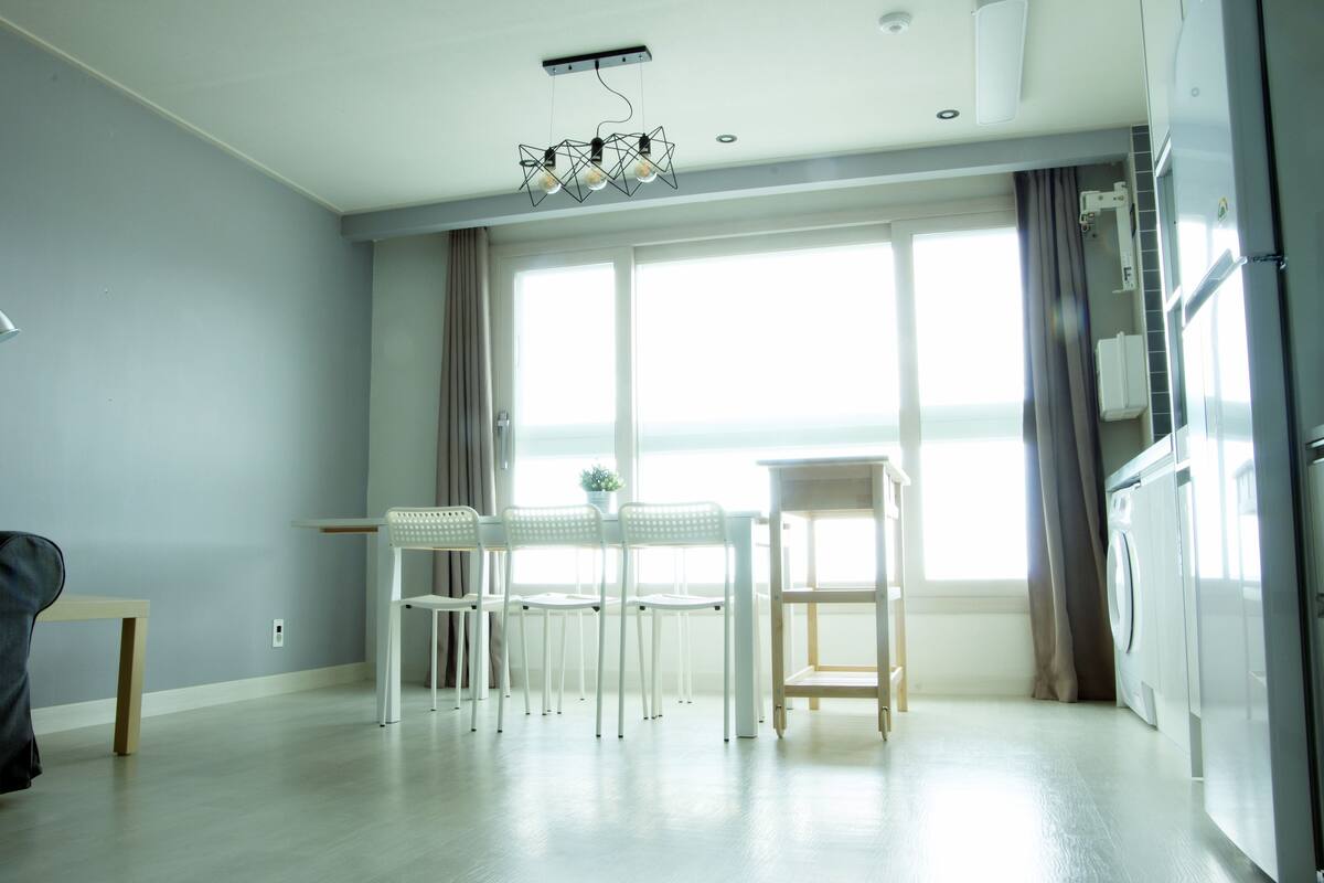 A modern kitchen with a dining area, large windows, and a washing machine.