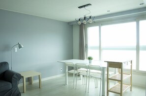 A modern living room with a white table, four white chairs, a grey sofa, a floor lamp, and a wooden shelf. - Terrace (Busan)