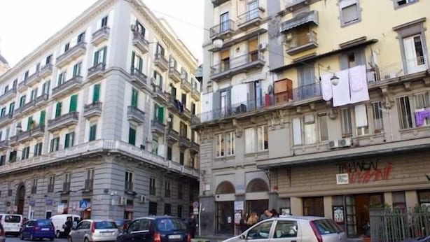 Vista de la calle de un edificio con varios pisos, balcones y coches estacionados.