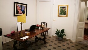 Una habitación con un escritorio de madera, una computadora portátil, un cuadro enmarco, una planta en maceta y una puerta.