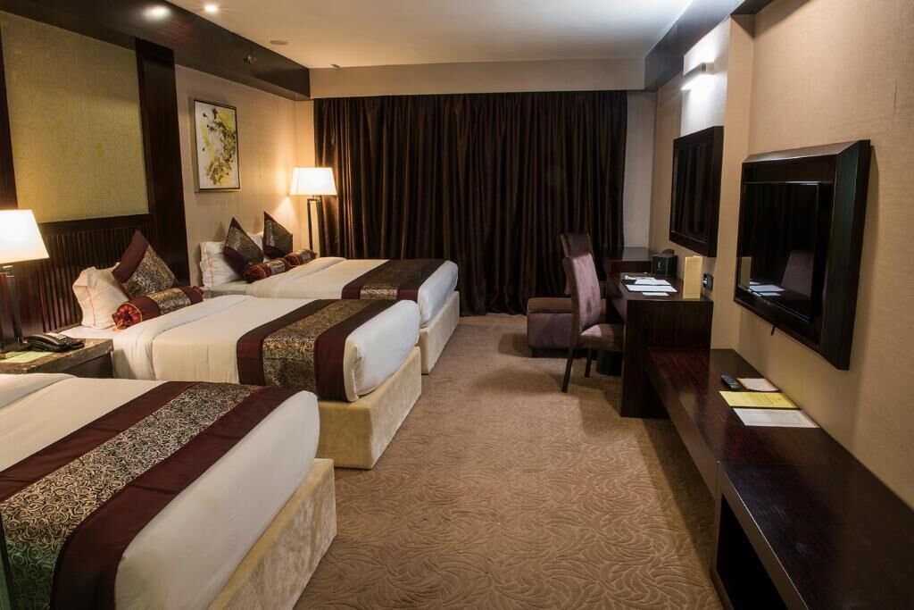 A hotel room with two beds, a desk, a chair, a television, and a large window with curtains.