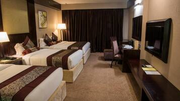 A hotel room with two beds, a desk, a chair, a television, and a large window with curtains.