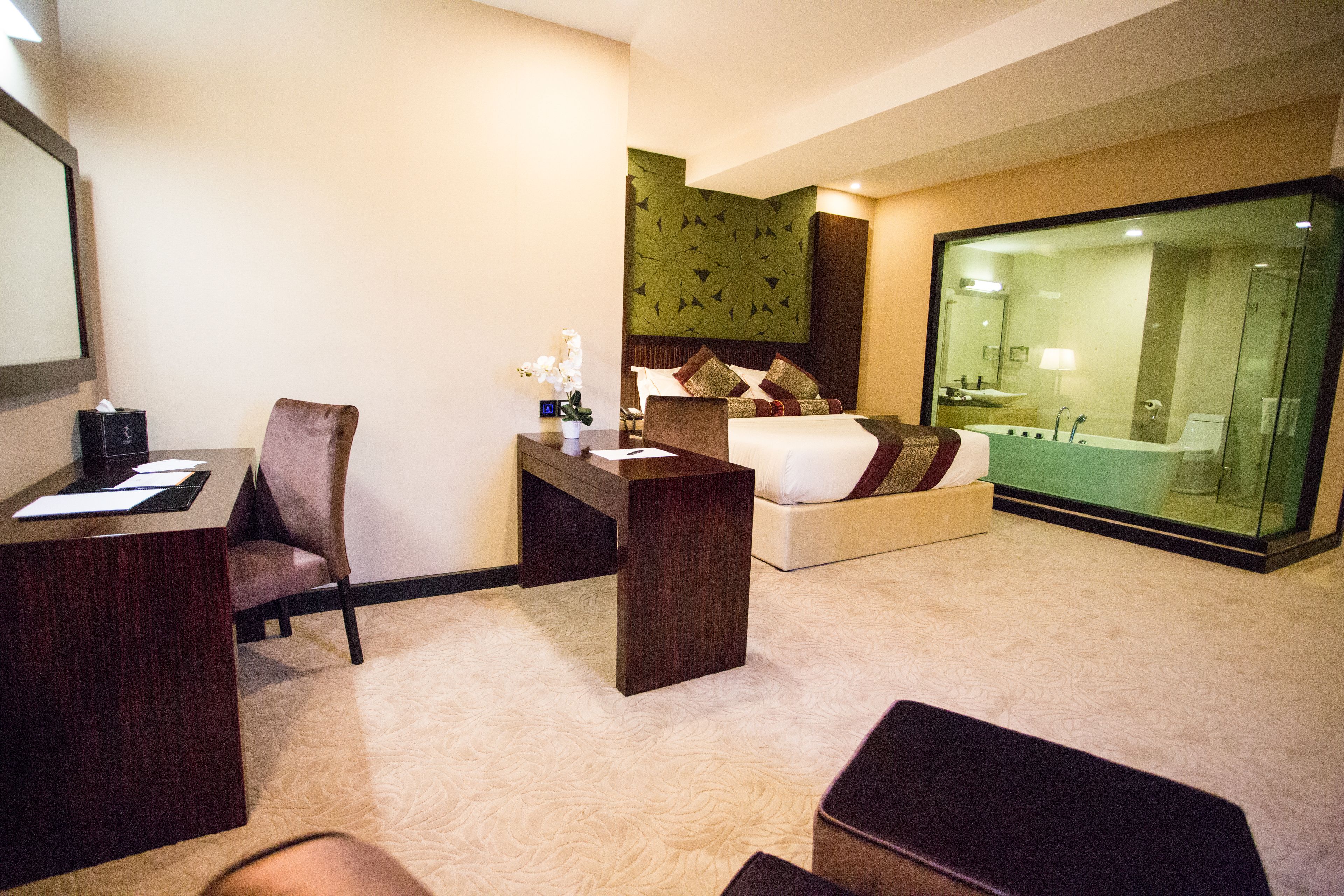 A hotel room with a desk, chair, bed, and a glass-enclosed shower area.