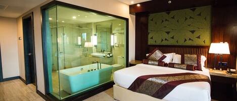 A modern hotel room with a large bed, a glass-enclosed bathroom, and a decorative wall panel.