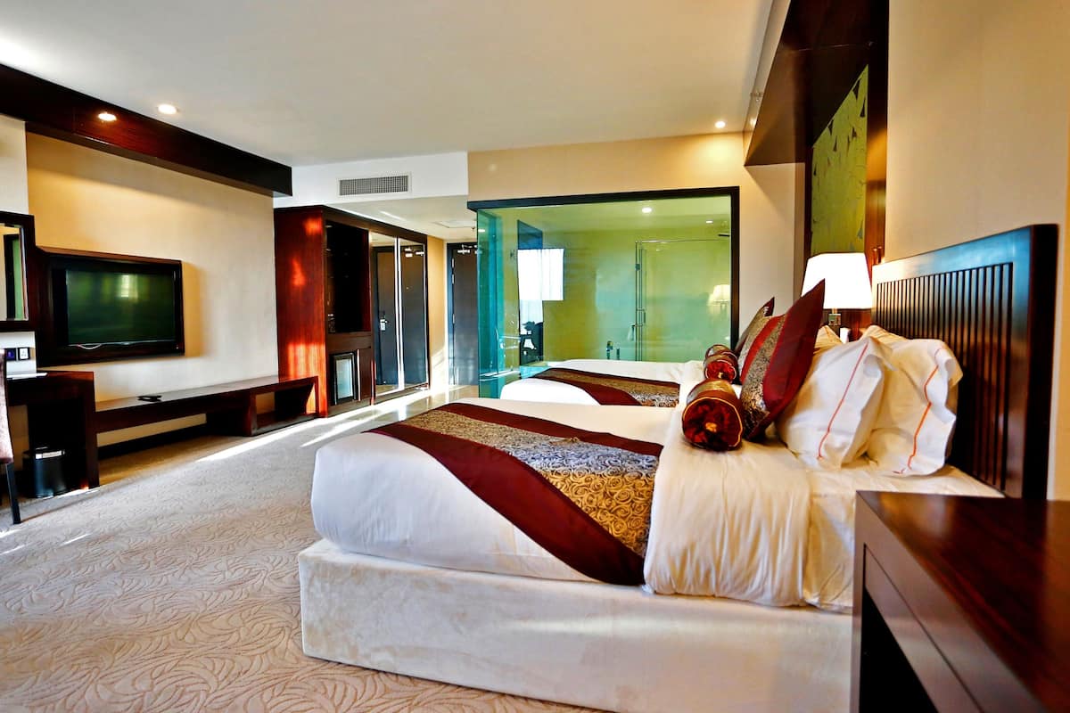 A hotel room with a large bed, a TV, a desk, and a glass wall.