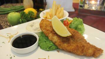 A plate with a breaded and fried item, possibly fish, accompanied by a slice of lemon, a side of fries, and a small bowl of sauce.