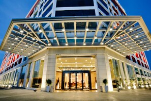 Una entrada de hotel moderna con toldo de cristal, ventanas amplias y fachada bien iluminada.