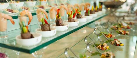 A buffet with various dishes, including shrimp, vegetables, and a variety of small plates.