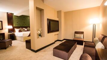 A hotel room with a bed, a TV, a sofa, a coffee table, and a lamp.