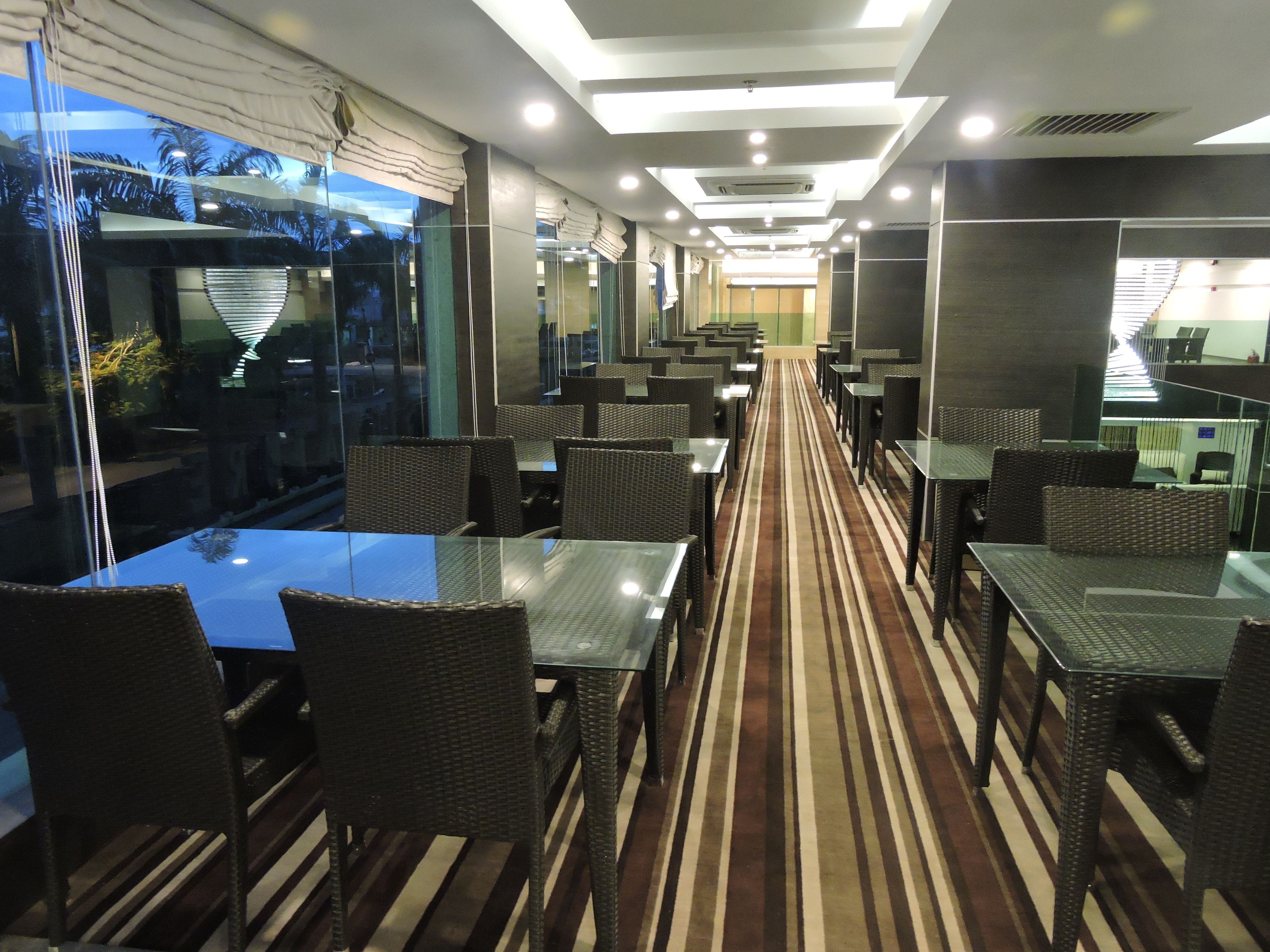 Un restaurante moderno con separaciones de vidrio, muebles de mimbre y una alfombra a rayas.