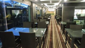 Un restaurante moderno con separaciones de vidrio, muebles de mimbre y una alfombra a rayas.