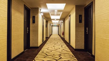 A hotel hallway with patterned carpet, doors on both sides, and a ceiling light.