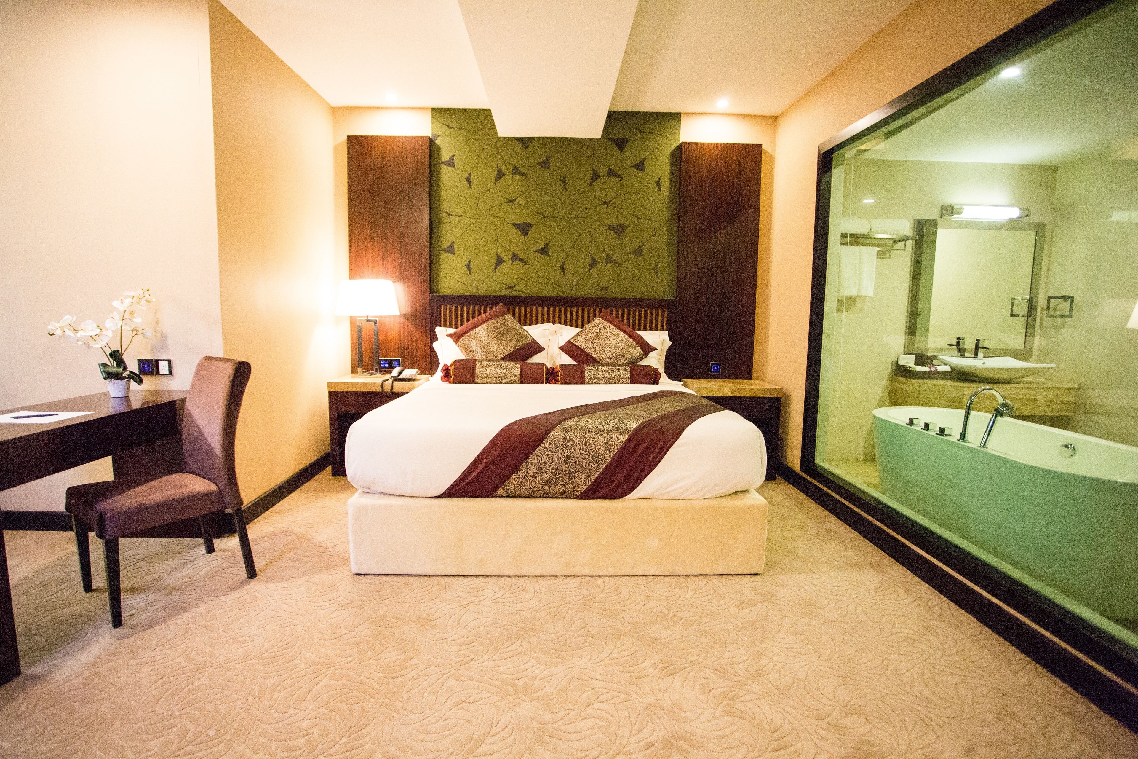 Una camera d'albergo con un letto grande, una scrivania con una sedia, un comodino e un bagno con cabina in vetro e vasca da bagno.