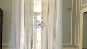 Una habitación con una mesa redonda, cortinas translúcidas y una lámpara de pie con diseño.