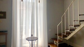 Una habitación con escalera, una mesa redonda con vela y cortinas de encaje.