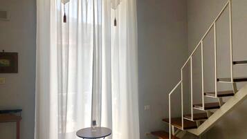 Una stanza con una scala, un tavolo rotondo con una candela e tende leggere.
