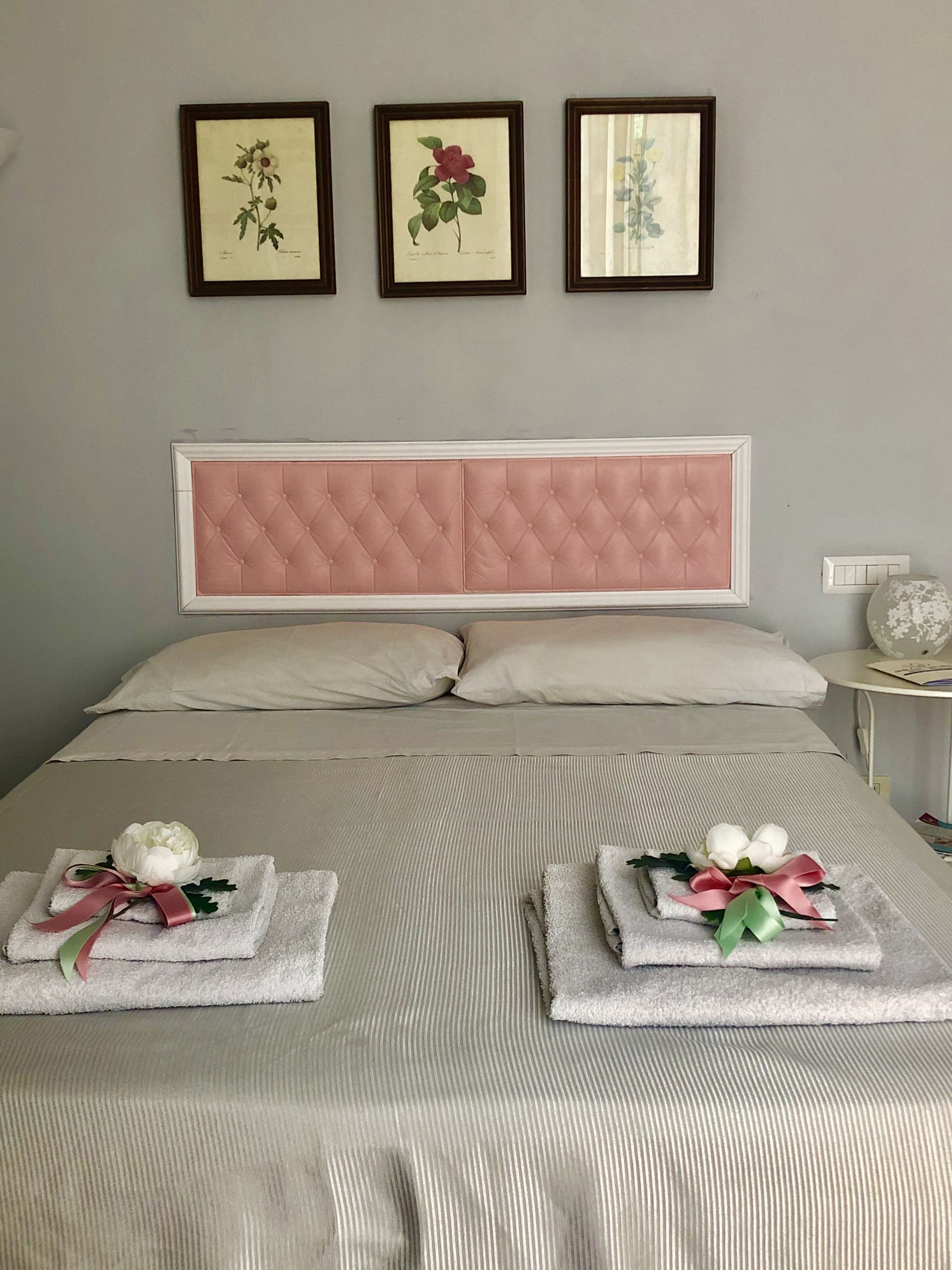 A neatly made bed with a pink tufted headboard, two pillows, and two towels with flowers and ribbons on the bed.