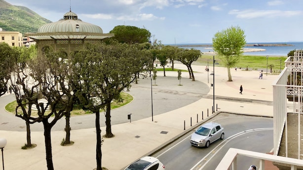 Vista de un paisaje urbano con una cúpula destacada, una carretera con coches y una masa de agua al fondo.