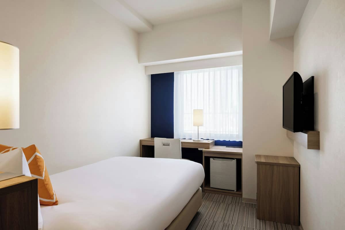 Une chambre d’hôtel avec un lit, un bureau, une chaise, une télévision et une fenêtre avec des rideaux.
