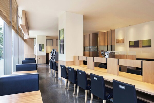 Un comedor moderno con mesas largas y sillas, una cocina al fondo y obras de arte en las paredes.