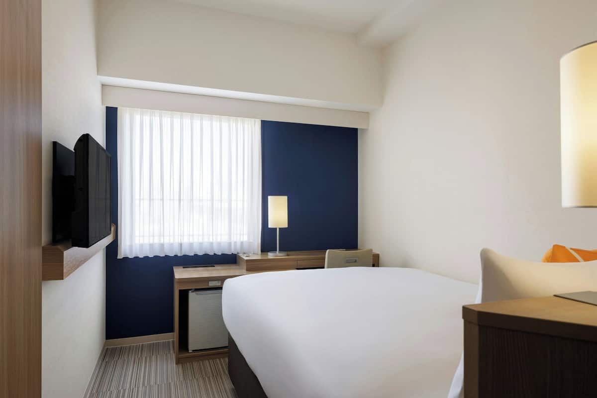 Une chambre d’hôtel avec un lit, un bureau, une télévision et une fenêtre avec des rideaux.
