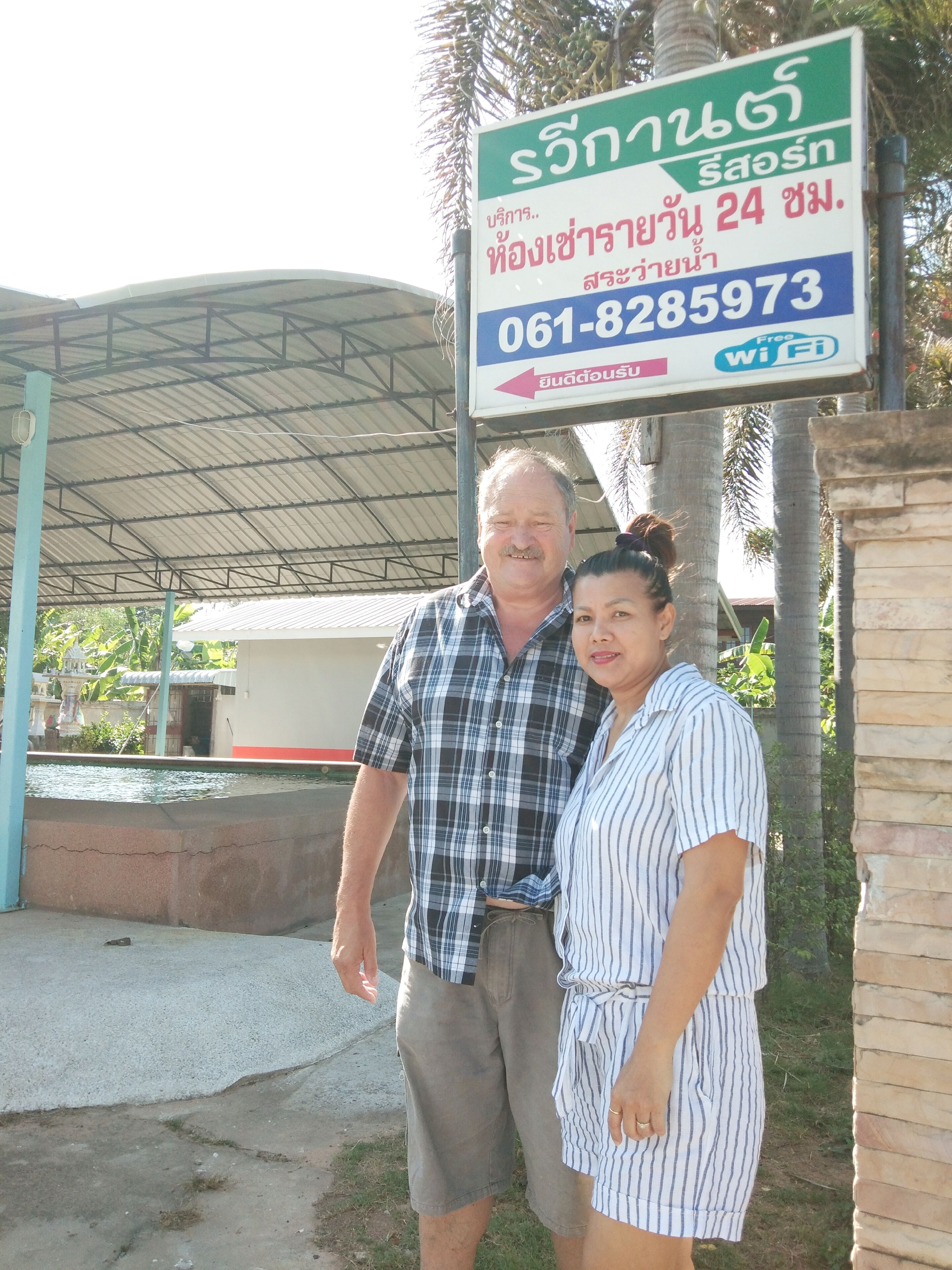 A couple standing in front of a sign with a phone number and a Wi-Fi symbol.