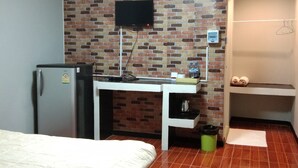 Camera d'albergo con un letto, una scrivania con televisore a schermo piatto, un frigorifero, parete con motivo a mattoni, pavimento piastrellato e piccolo bagno con lavandino e portasci.